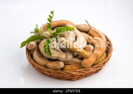 Tamarind  bean like pods filled with seeds surrounded by a fibrous pulp arranged in a basket with white textured background. Stock Photo