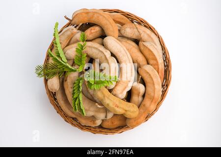 Tamarind  bean like pods filled with seeds surrounded by a fibrous pulp arranged in a basket with white textured background. Stock Photo