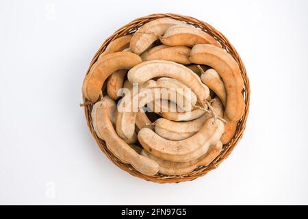 Tamarind  bean like pods filled with seeds surrounded by a fibrous pulp arranged in a basket with white textured background. Stock Photo