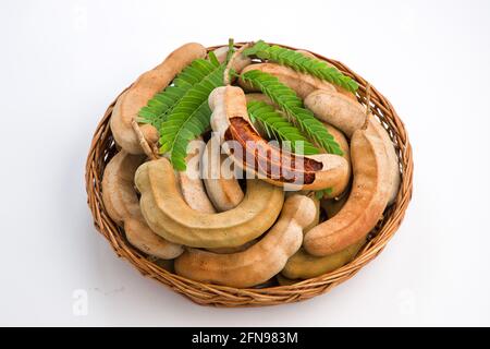 Tamarind  bean like pods filled with seeds surrounded by a fibrous pulp arranged in a basket with white textured background. Stock Photo