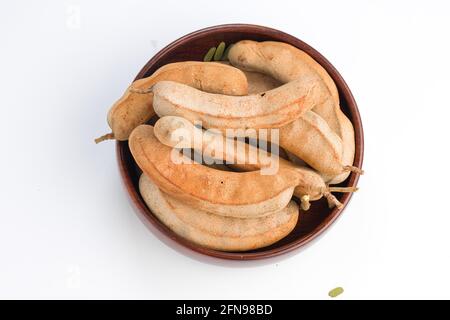 Tamarind  bean like pods filled with seeds surrounded by a fibrous pulp arranged in a basket with white textured background. Stock Photo