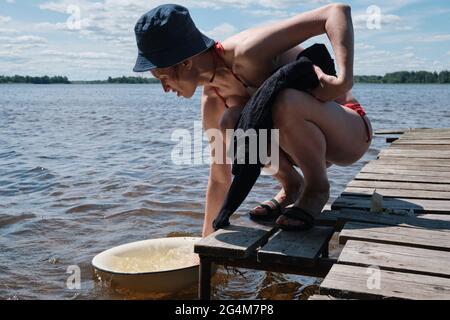 Young girl washes clothes by hand in basin. Hand wash clothes in nature. Washing clothes in the lake. Stock Photo