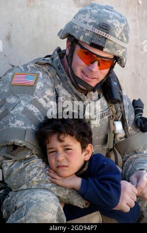 US Army (USA) Corporal (CPL) James Reinhard, Vipers Task Force (TF), Headquarters/Headquarters Detachment (HHD), 519th Military Police (MP) Company (MP Co), comforts 5-year old Okmed outside of an Iraqi Police (IP) station in Baghdad, Baghdad Province, Iraq (IRQ), while taking a break from training and assisting IP officers during Operation IRAQI FREEDOM.  (US NAVY PHOTO BY PH1 (AW) BART A BAUER 060312-N-7586B-202) Stock Photo