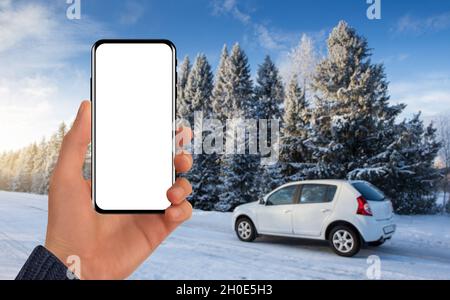 Hand with a phone on the background of a car behind a winter road. Blank screen, you can add your content Stock Photo