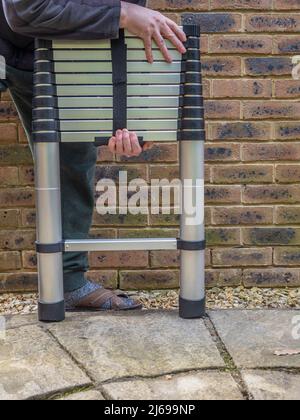 Man holding Aluminium tubular section telescopic access ladder collapsed down for storage Stock Photo