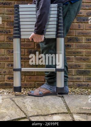 Man carrying an Aluminium tubular section telescopic access ladder Stock Photo