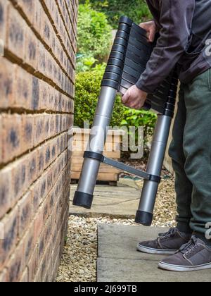 Man positioning alumimium tubular ladder to extend before carrying out some decorating Stock Photo