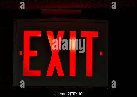 An exit sign over a doorway to the outside in a dark hallway. Stock Photo