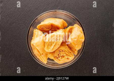 Several pieces of sweet honey baklava in a glass bowl on a slate stone, close-up, top view. Stock Photo