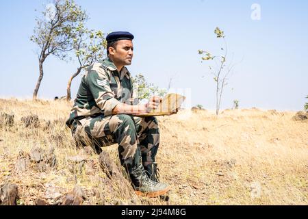 soldier seriously checking map while sitting on top mountain - concept of strategy planning, intelligence gathering and monitoring Stock Photo