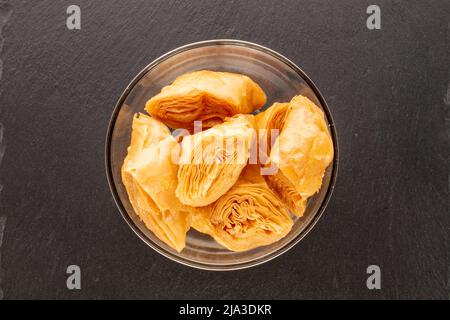 Several pieces of sweet honey baklava in a glass bowl on a slate stone, close-up, top view. Stock Photo