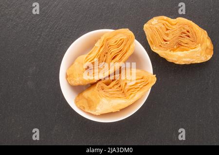 Three pieces of sweet honey baklava with a white saucer on a slate stone, close-up, top view. Stock Photo