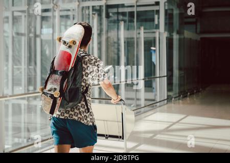 Young man walking at the airport with skateboard on his back. Stock Photo