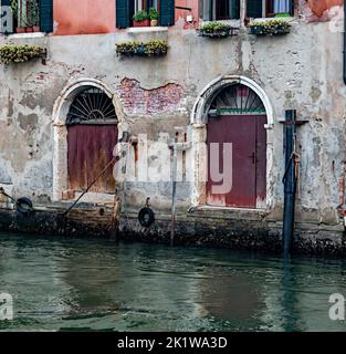 Close up of ancient Facade of an old colorful building with doors and windows on a canal with water reflection in Venice, Italy. Stock Photo