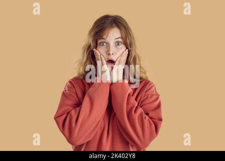 Portrait of young amazed woman with wide opened eyes and open mouth with hands on face. Stock Photo