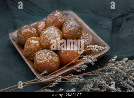 Three flavored preserved chinese plums (Preserved fruits) on wooden plate. Its flavour has sour, salty and sweet taste. Space for text, Selective Focu Stock Photo