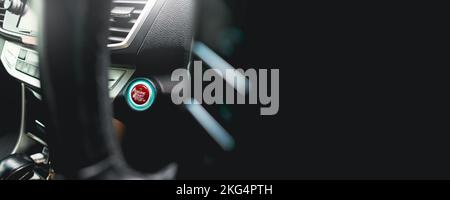 Red engine start stop button with an LED blue light on panel in a automobile , horizontal banner copy space on black background Stock Photo