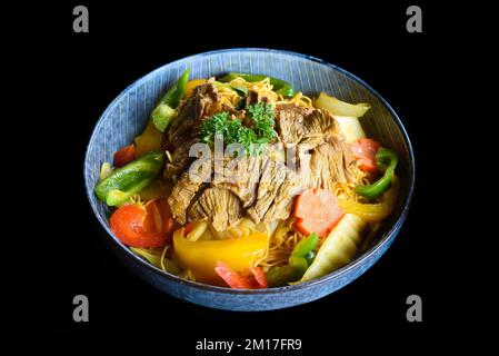 Stewed beef with noodles and vegetables in a blue bowl isolated on black background top view Stock Photo