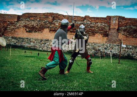 Sword fight of two knights in helmets and chain mail armor in scenery of medieval castle Stock Photo