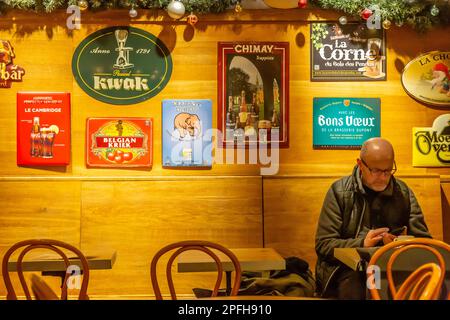 Man sitting in a café in Brussels, consulting his mobile phone in front of a cup of coffee. Advertisements for Belgian beers hang on the wall behind h Stock Photo