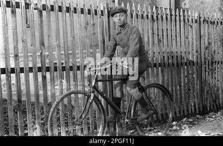 1920s, historical, a young lad, possibly a schoolboy, in shorts and flat cap, sitting on his bicycle for his photo beside a wooden fence, England, UK. Stock Photo