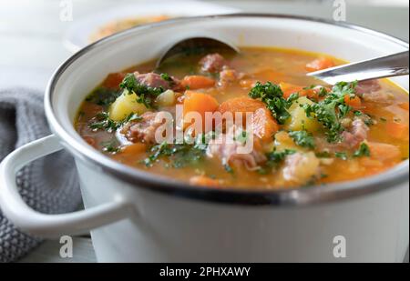 Stew with carrots, potatoes and smoked pork meat in a white enamel pot. Stock Photo