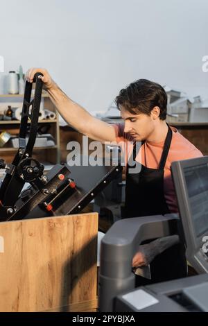 man in apron using professional print plotter while working in print center,stock image Stock Photo