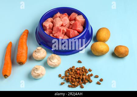 Bowl with raw meat, dry pet food and natural products on blue background Stock Photo