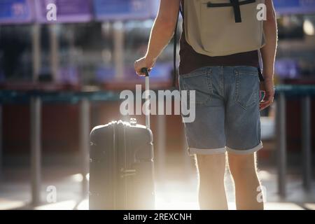 Traveling by airplane. Selective focus on hand of man holding suitcase. Traveler walking with luggage through airport terminal towards check-in. Stock Photo