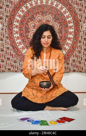 A woman practicing meditation and healing with a Tibetan singing bowl. Human body 7 Chakras energy system pictures, yoga meditation. Stock Photo