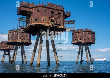 The Maunsell Forts seen with very serious structural defects and many of their parts fallen into the sea. Nowadays only the seagulls nest in them. A ferry boat is visible at the distance as this water is not safe for boating. The Maunsell Forts are armed towers built at the Thames and the Mersey Estuaries during the Second World War to defend the United Kingdom. They have been built 1942 - 1943 for anti-aircraft defense and to report to London about the German aircraft. They are all named after the designer Guy Maunsell. Stock Photo