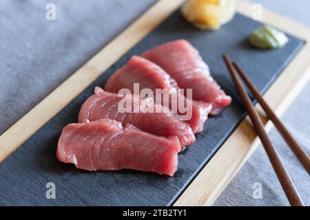 Japanese style home eating - homemade raw Akami tuna sashimi on a slate serving board with wooden chopsticks, ginger and wasabi. UK Stock Photo