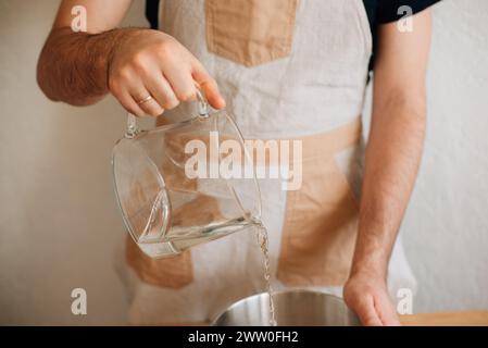 male baker pours water into a bowl of flour. High quality photo Stock Photo