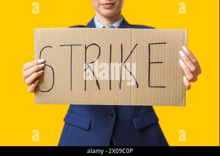 Protesting female stewardess holding placard with text STRIKE on yellow background Stock Photo