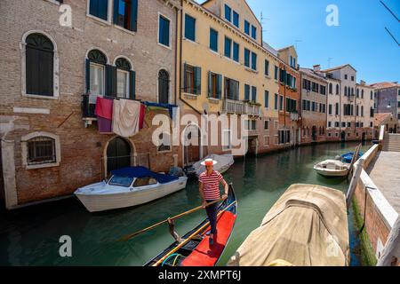 Venice, Italy - June 05, 2024: Gondolier in Red Striped Shirt on Venice Canal. Stock Photo