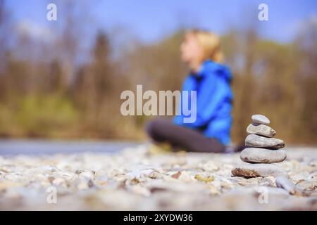 Cairn on a pebble beach, meditating woman in the background Stock Photo