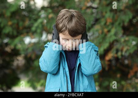 Autism concept. Lonely little boy covering his ears outdoors Stock Photo