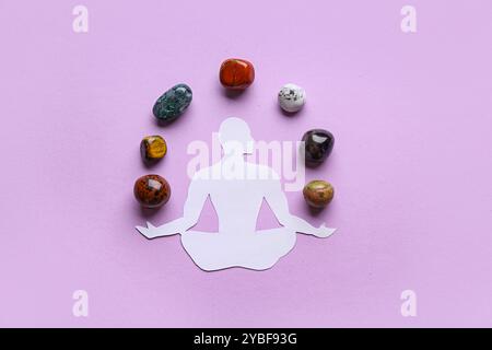 Set of chakra stones and paper figure of meditating human on lilac background Stock Photo