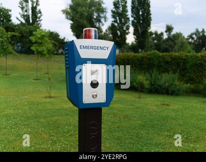 Red emergency police SOS call button with light panel, CCTV camera and speaker for urgent communication with the police in a city park. Civil security Stock Photo