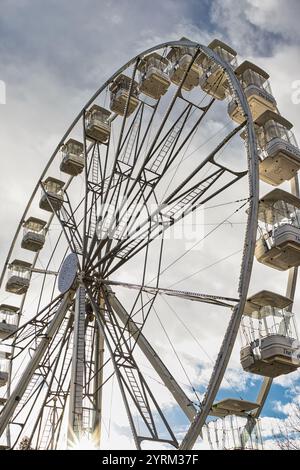 A low-angle view of a Ferris wheel against a cloudy sky. The wheel is predominantly gray and white, with numerous passenger gondolas labeled 'The View Stock Photo