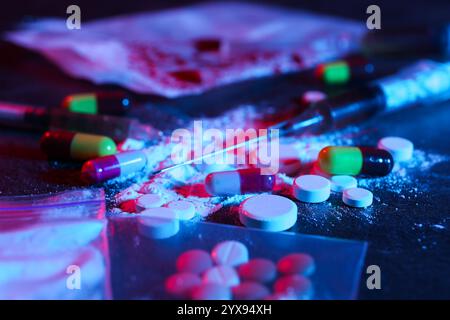 Drug addiction. Different pills, powder and syringe on dark table in neon lights, closeup Stock Photo