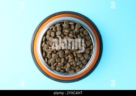 Dry pet food in feeding bowl on light blue background, top view Stock Photo