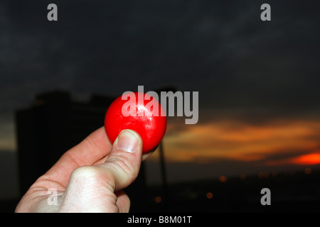 Red, wax enclosed encased cheese wheel in fingers with background sunset Stock Photo