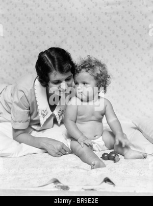 1920s 1930s WOMAN MOTHER LYING SITTING WITH BABY ON BLANKET Stock Photo