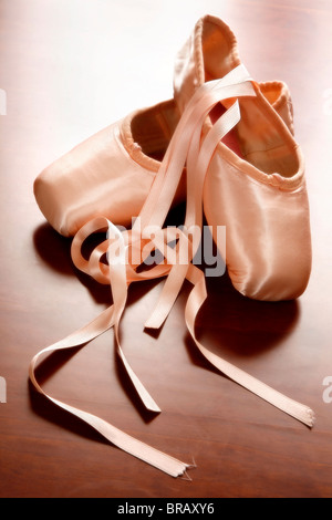 Pink satin ballet shoes on dark floor Stock Photo