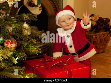 A baby santa standing next to a present Stock Photo