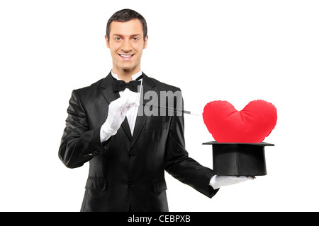 Young magician holding a magic wand and top hat with a red heart shaped pillow in it isolated on white background Stock Photo