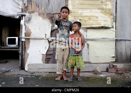 Two young Asian boys living in poverty are standing in front of a squatters home on a city street in Kampong Cham, Cambodia Stock Photo