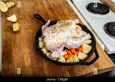 A raw chicken prepared for roasting with potatoes and carrots in a cast iron frying pan Stock Photo