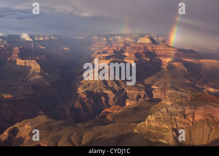 A storm at sunset creates a double rainbow over Plateau Point viewed from Yavapai Point on the South Rim Stock Photo